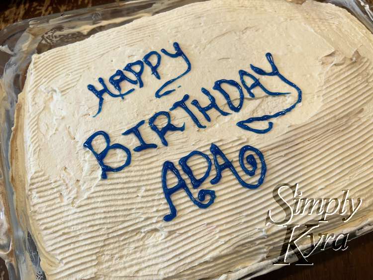 Closeup view of the top of the cake with lines in the top and blue letters saying "HAPPY BIRTHDAY ADA".