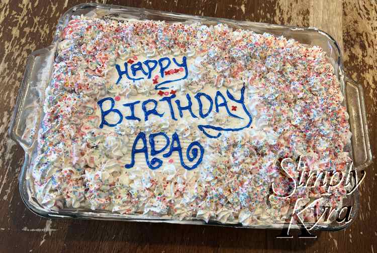 Image shows the actual final cake coated in pastel colors, pink and red Xs and Os, and the birthday message. 