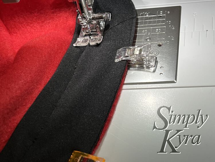 Image shows the edge of the hat top under the sewing machine's foot as it's being stitched into place about half a centimeter from the top of the band.