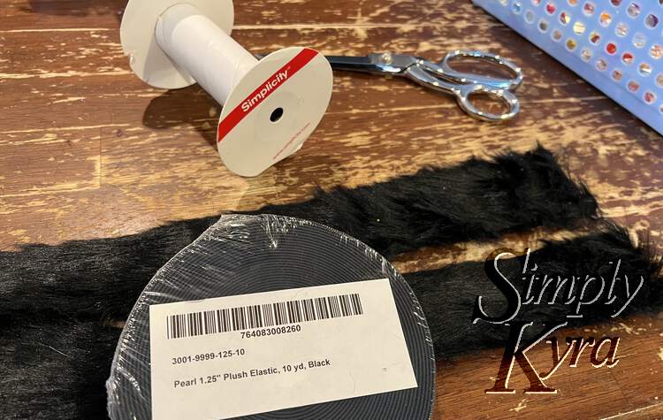 Image shows the ends of the fur trim so it looks like two pieces. On top of it lays the unopened plush elastic and behind it lays the empty cardboard spool and my scissors. 
