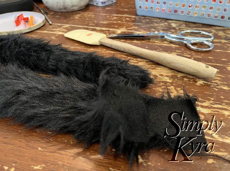 Image shows both ends of the tail as the tail was folded in half (off screen). In the front is the open end with the two flaps opened. In the back you can see the tip of the tail ending at a point. Behind all that are my spatula, scissors, sewing clips, and a basket. 