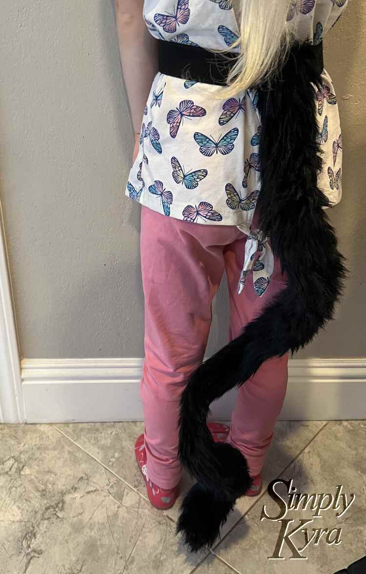 Image shows the back of Zoey while wearing the tail around her waist. The tail itself is spiraled at the bottom and curved near the top so it barely brushes the floor.