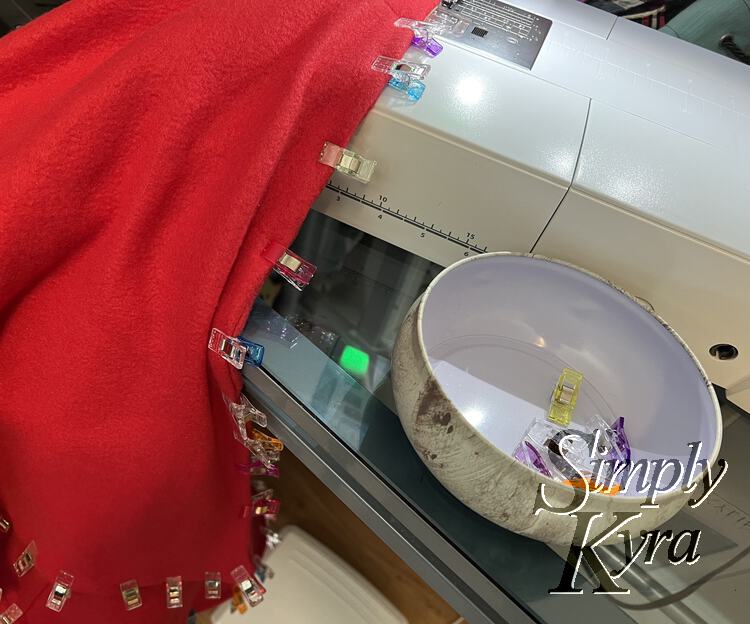 Image shows the jacket under the sewing machine foot with sewing clips all the way along the edge. 