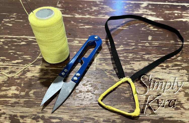 Image shows the finished necklace with the scissors and thread off to the side. All is laid out on the wooden table. 