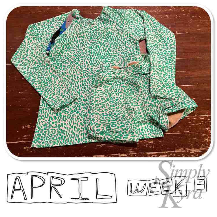 Image shows a flat lay of Ada's cheetah print swim suit consisting of a long sleeved raglan and matching shorts. There's sharks where the Kamsnaps were placed on the placket. Below it says "April Week 3".