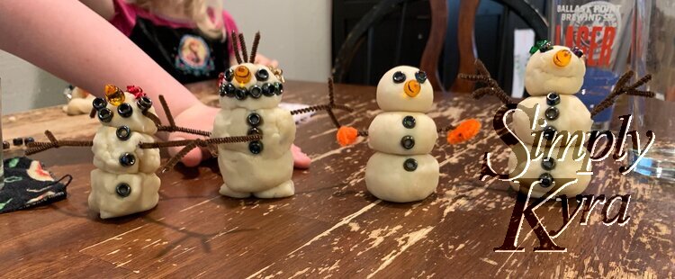 All four snow people all lined up for the photo. In the background you can see Ada's arm and Zoey's body.