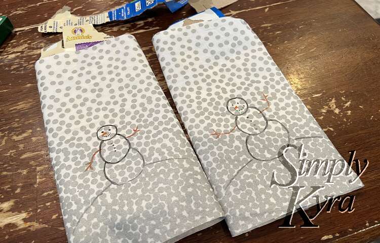Image shows the two recently started bags side by side with a snow person on a hill waving at the viewer. The fabric itself is positioned so the bottom is mostly silver while the top is white. 