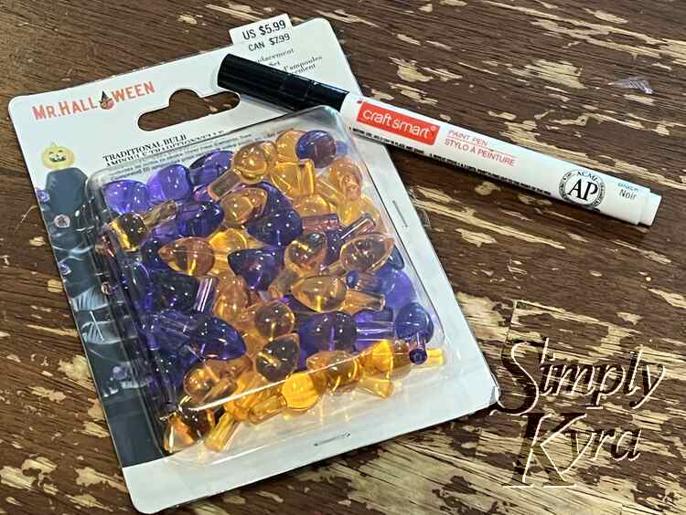 Image shows the closed package of Mr Halloween Tradition Bulbs half purple and half orange. A fine tipped paint pen sits to the side. 
