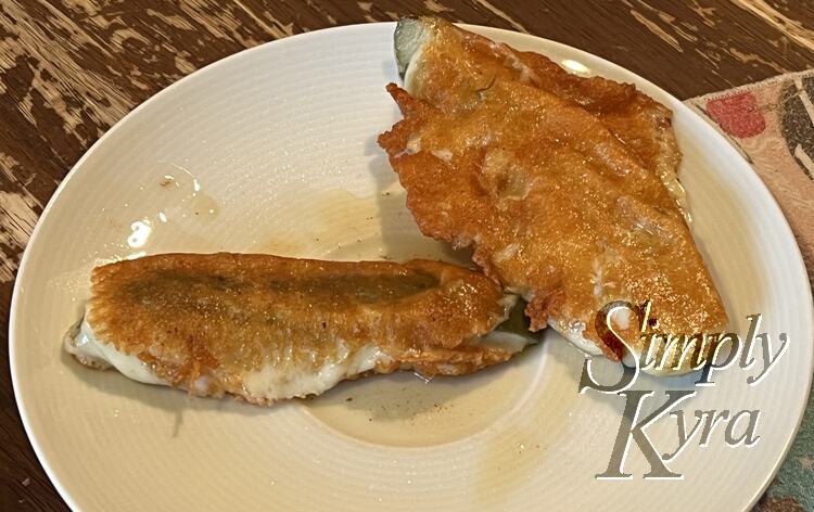 Image shows two vaguely pickle shaped items on a plate with a napkin of to the side. The green pickle sticks out the end and there's an odd white spot amid the orange-browned cheese outer shell. 