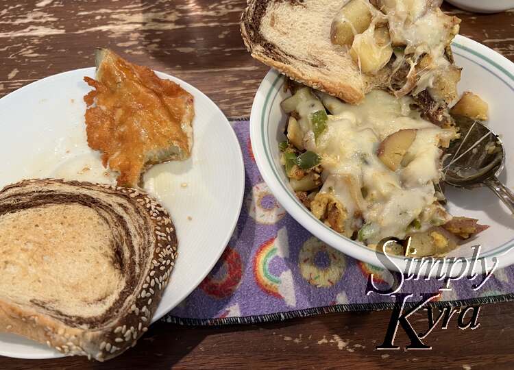 Image shows a bowl of leftovers with melted cheese on top to the right and a plate with a half eaten fried and cheesy pickle on the left. On either dish there's marbled rye toast. 