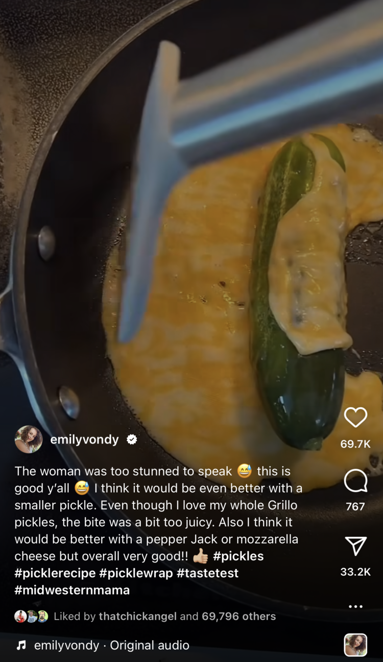 Image is now dimmed as the bottom of the screenshot shows emilyvonder's info along with the caption of the video post. The screenshot itself shows a marbled cheese on a frying pan with a pickle in the center and some cheese being scraped up to wrap around it.